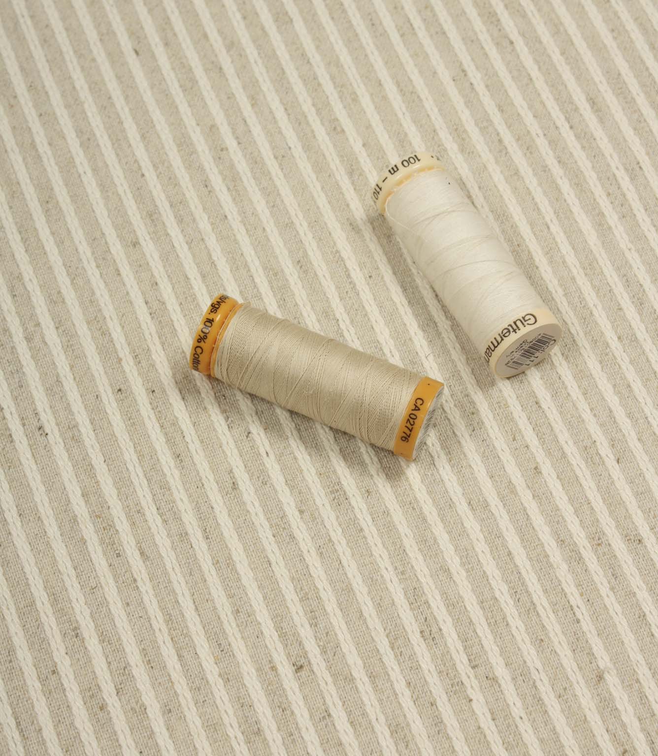 Wedmore Wide striped upholstery fabric displayed with coordinating thread spools, highlighting its woven texture and subtle stripe detailing.