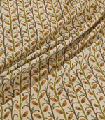 Wildwood Amber fabric draped in soft folds, showing the repeating small-scale leaf pattern in warm ochre, olive green, brown and muted blue on a natural cream ground.