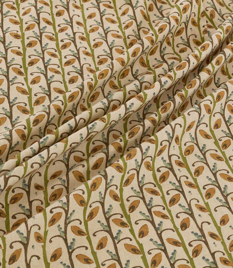 Wildwood Amber fabric draped in soft folds, showing the repeating small-scale leaf pattern in warm ochre, olive green, brown and muted blue on a natural cream ground.