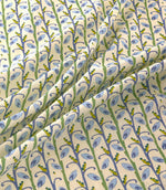 Wildwood Saltwater fabric draped in soft folds, showing the repeating small-scale botanical pattern of blue leaves, green stems and mustard yellow accents on a natural cream ground.