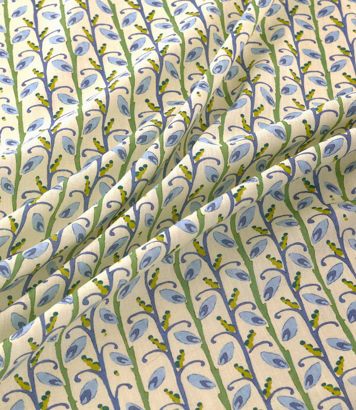 Wildwood Saltwater fabric draped in soft folds, showing the repeating small-scale botanical pattern of blue leaves, green stems and mustard yellow accents on a natural cream ground.