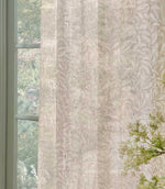 Close-up of William Morris Pure Willow Boughs sheer curtain fabric in a soft linen beige and ivory colourway, gently filtering natural light beside a green painted window.