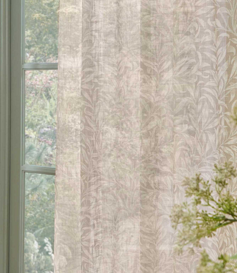 Close-up of William Morris Pure Willow Boughs sheer curtain fabric in a soft linen beige and ivory colourway, gently filtering natural light beside a green painted window.
