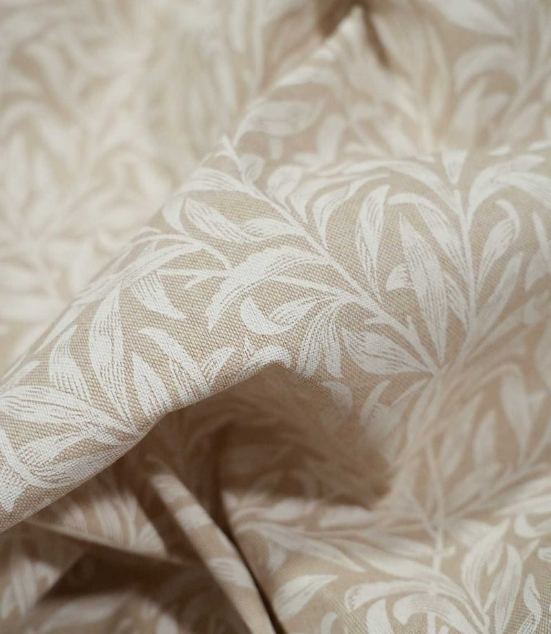 Close-up of draped Willow Bough Linen Look fabric in beige and cream, highlighting the flowing leaves, woven texture and natural movement of the material.