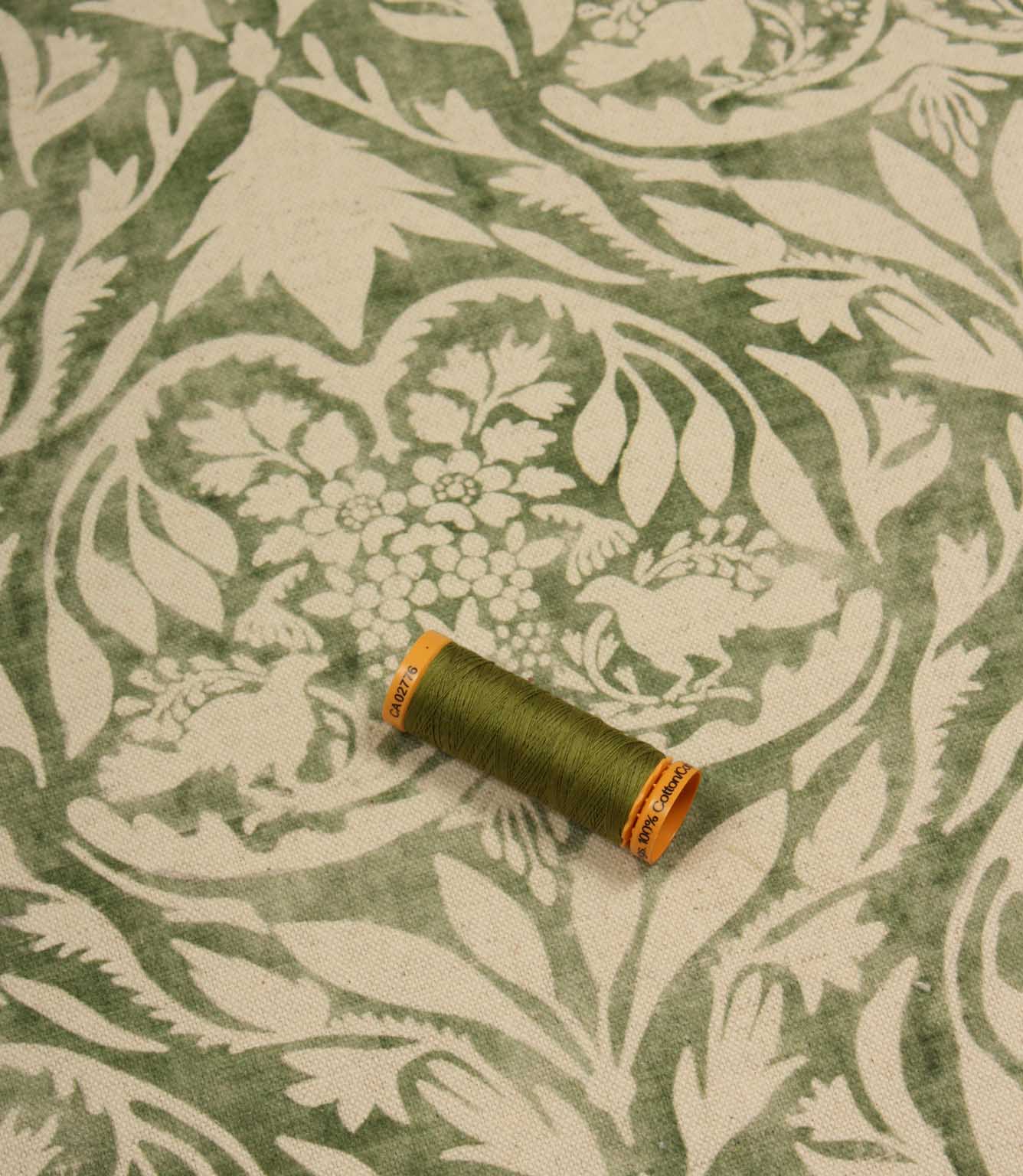 Spool of green thread on a patterned fabric background