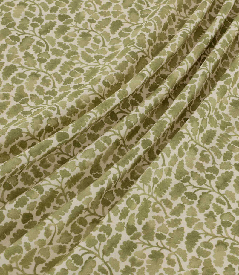 Woodcliff Kelp fabric arranged in soft, flowing folds, showing its delicate Scandinavian-style botanical design with olive and sage green leaves, intertwining branches and a warm cream background.