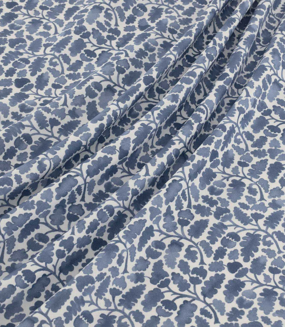 Woodcliff Nautica fabric arranged in soft, flowing folds, showcasing its repeating oak leaf and acorn design in navy and dusty blue tones on an ivory background, with a finely woven texture and delicate foliage detailing.