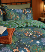 Close-up of the navy Woodland Ritual duvet cover and pillowcase, showing colourful woodland trees, deer, foxes, owls and celestial details with the green leafy reverse folded back.