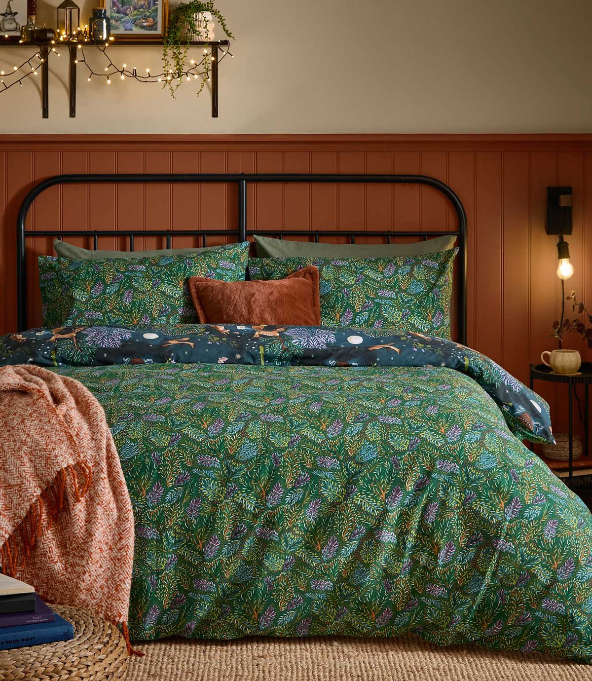 Woodland Ritual reversible duvet cover displayed on its green botanical reverse with dense blue, purple and rust foliage, with the navy woodland animal print folded back across the bed.