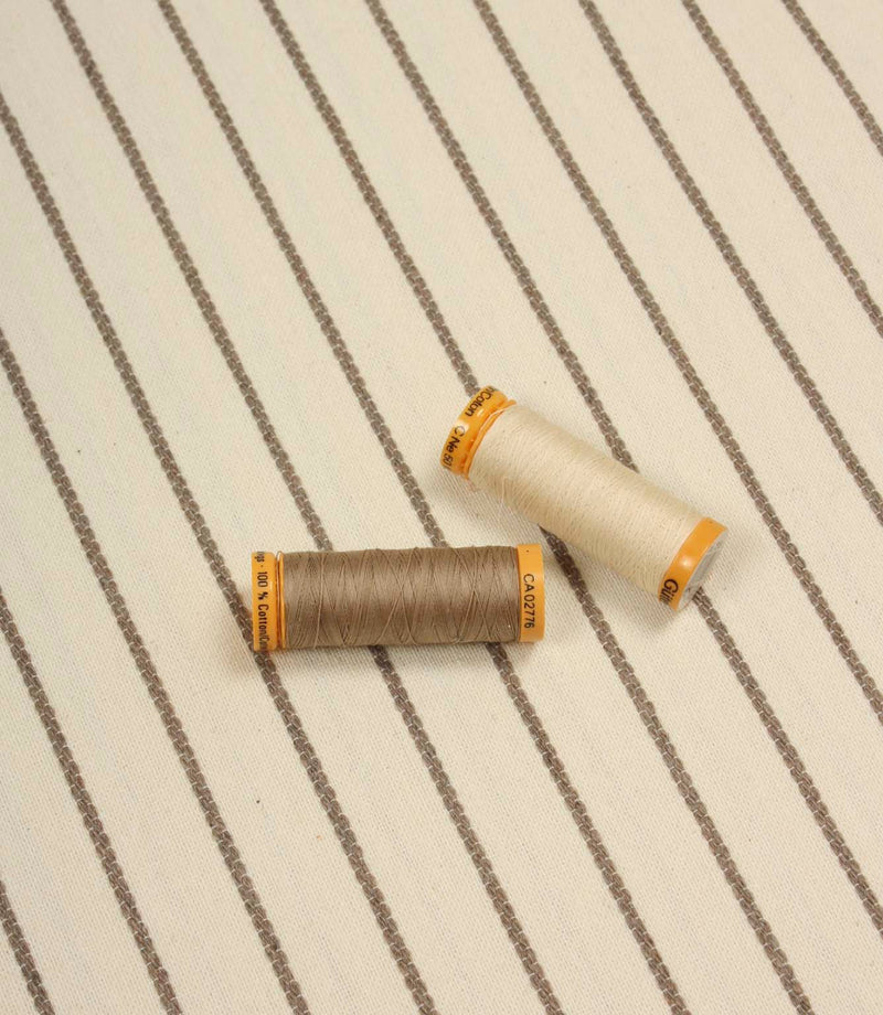 Wooton Wide striped upholstery fabric displayed with coordinating thread spool, highlighting its woven texture and embroidered detailing.