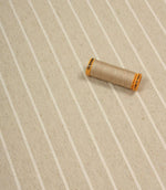 Wooton Wide striped woven fabric displayed with coordinating thread spool, highlighting its soft upholstery texture.