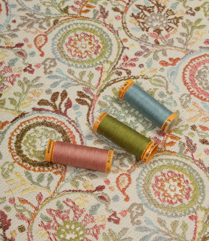 Wychwood Jasmine fabric displayed with coordinating blue, green and blush pink thread spools highlighting the woven floral design.