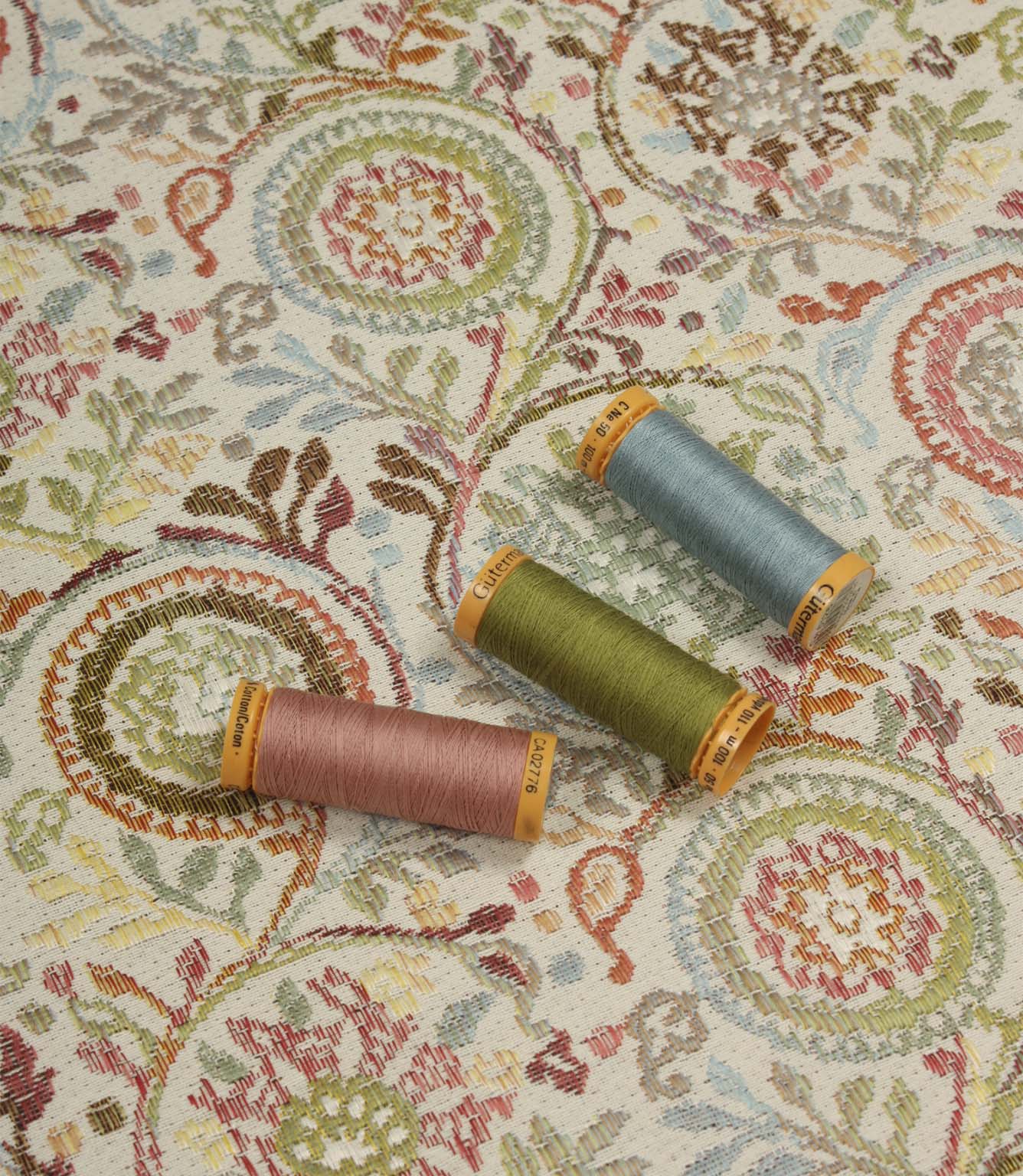 Wychwood Jasmine fabric displayed with coordinating blue, green and blush pink thread spools highlighting the woven floral design.