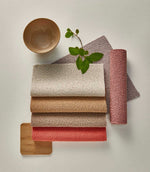 Camira Yoredale wool bouclé upholstery fabric samples arranged in cream, oatmeal, warm tan, taupe, coral pink and soft mauve, showing the collection's tactile looped texture.