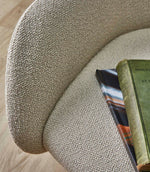 Close-up of an upholstered chair covered in Camira Yoredale wool bouclé fabric in a warm natural beige tone, showing the softly textured weave across the curved seat and back.