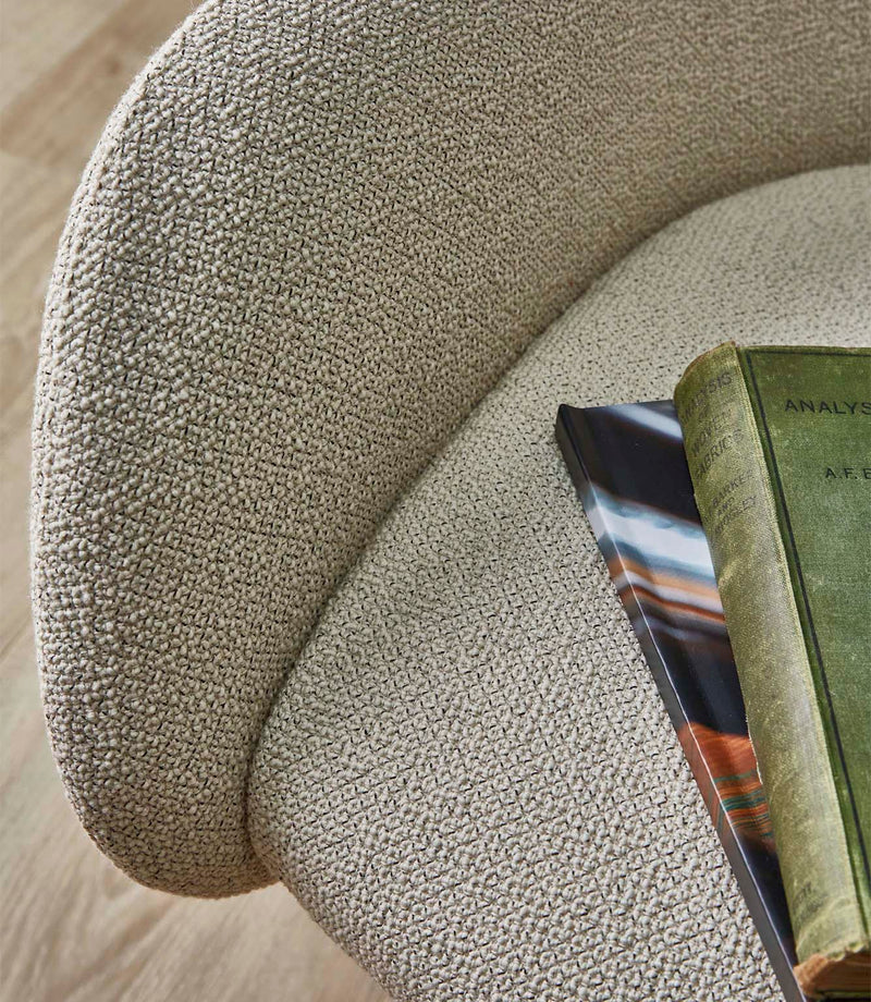 Close-up of an upholstered chair covered in Camira Yoredale wool bouclé fabric in a warm natural beige tone, showing the softly textured weave across the curved seat and back.
