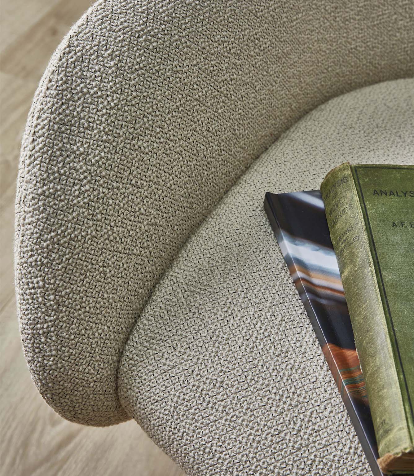 Close-up of an upholstered chair covered in Camira Yoredale wool bouclé fabric in a warm natural beige tone, showing the softly textured weave across the curved seat and back.