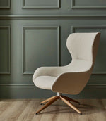 Contemporary high-back lounge chair upholstered in Camira Yoredale wool bouclé fabric in a light cream tone, set against muted sage green panelled walls with a wooden floor.