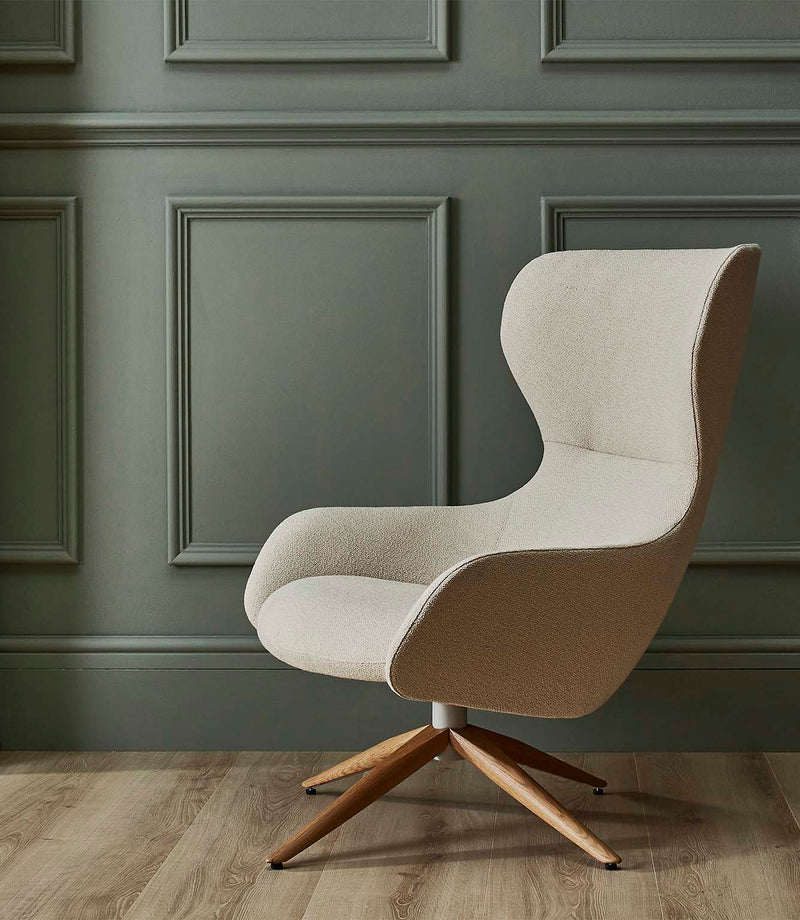 Contemporary high-back lounge chair upholstered in Camira Yoredale wool bouclé fabric in a light cream tone, set against muted sage green panelled walls with a wooden floor.