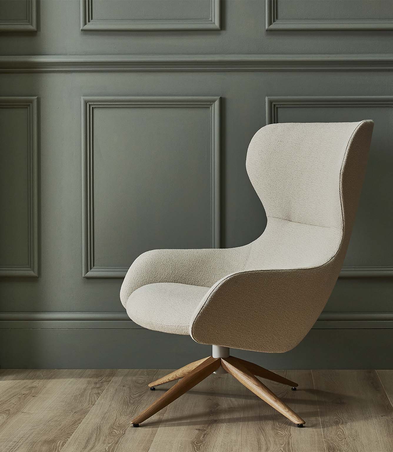 Contemporary high-back lounge chair upholstered in Camira Yoredale wool bouclé fabric in a light cream tone, set against muted sage green panelled walls with a wooden floor.